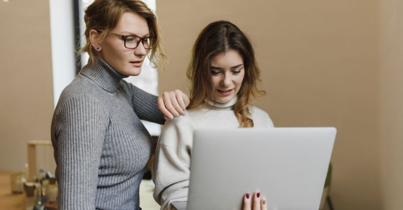 Managing Freelancers - Woman in Gray Sweater Looking at the Screen of a Laptop the Woman in Beige Sweater is Holding