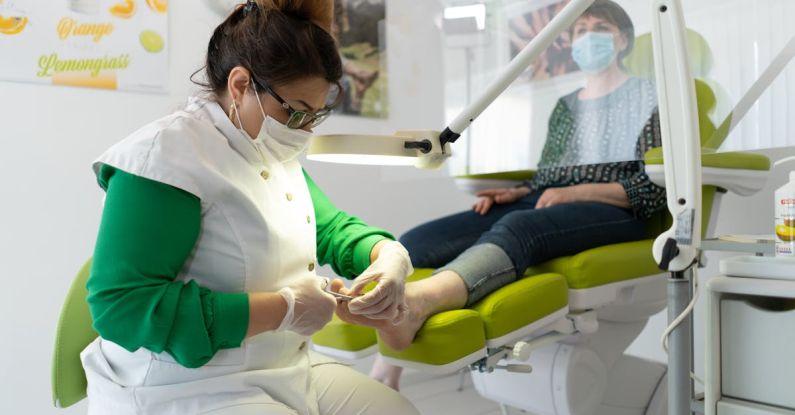 Employee Wellness - Concentrated professional master in beauty salon wearing medical mask doing pedicure during coronavirus epidemic