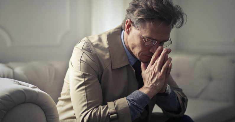 Financial Stress - Side view of upset male entrepreneur in formal wear sitting on couch in modern living room and contemplating about financial problems while leaning on hands and looking down