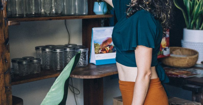 Sustainable Marketing - Woman Picking Up a Cup on Brown Wooden Shelf